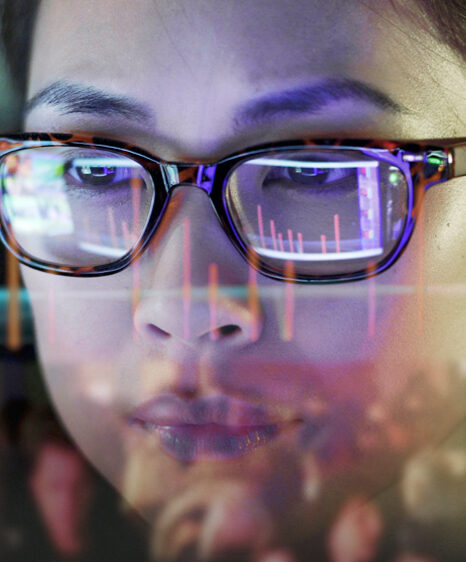 A young girl wearing glasses looking at a screen with column charts that are reflecting in her glasses.