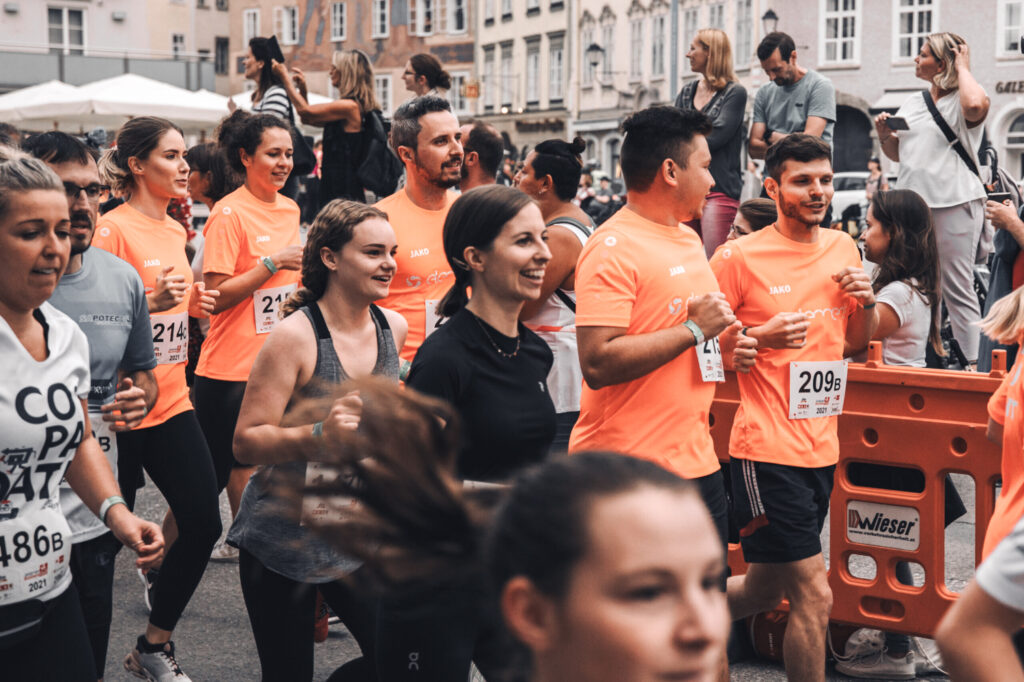 Eine Gruppe Läufer*innen beim Salzburg Business-Lauf. In der Mitte laufen einige elements-Mitarbeitende in orangen Sportshirts.
