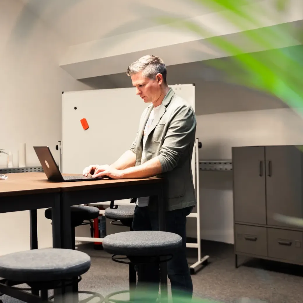 Photo of a man standing at a high table and working on a laptop.