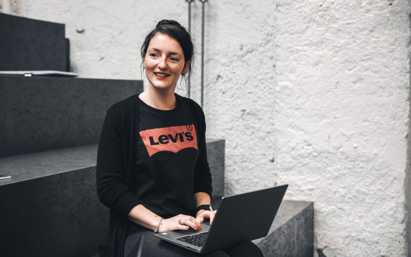 valantic Austria Mitarbeiterin, die auf einer Stufe sitzt und an ihrem Laptop arbeitet.