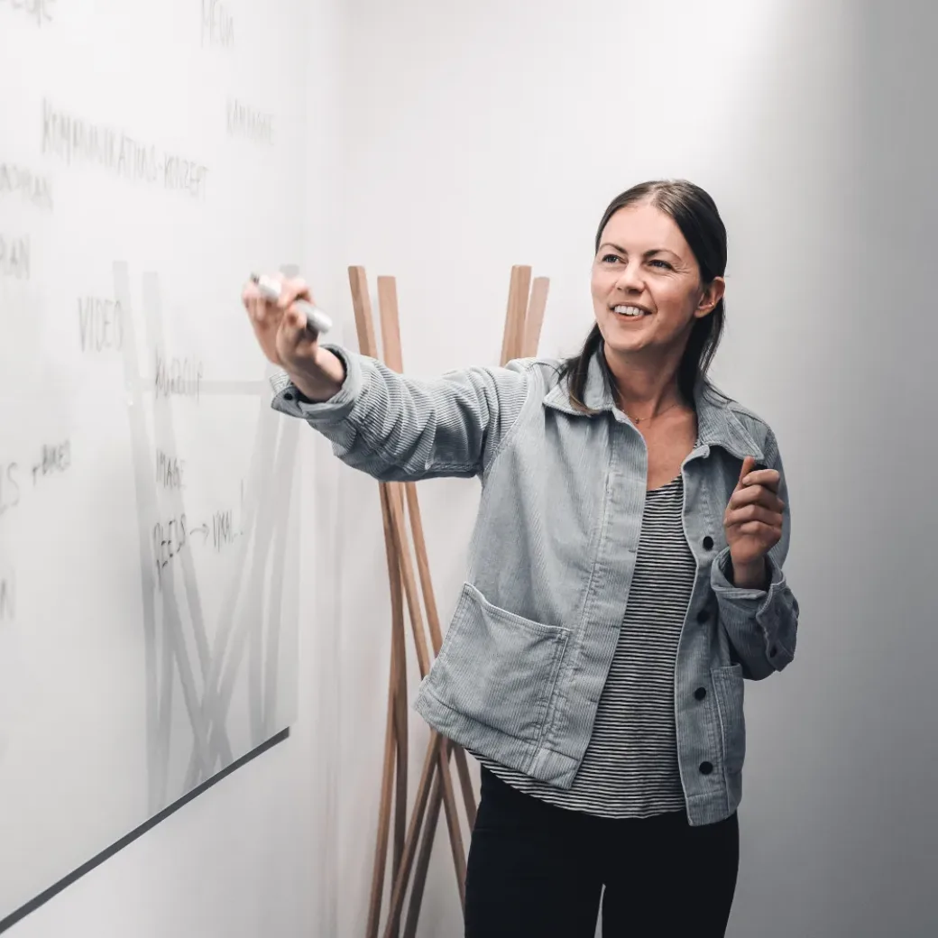 Junge Frau präsentiert Projetkidee an einem White Board.
