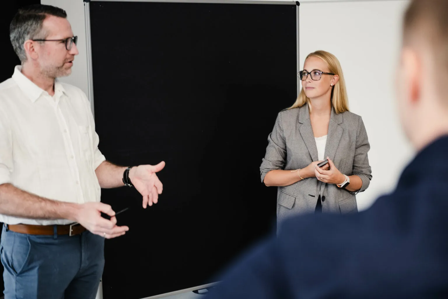Two people are presenting at the CRM roundtable in front of a black pinboard while participants listen in the foreground.