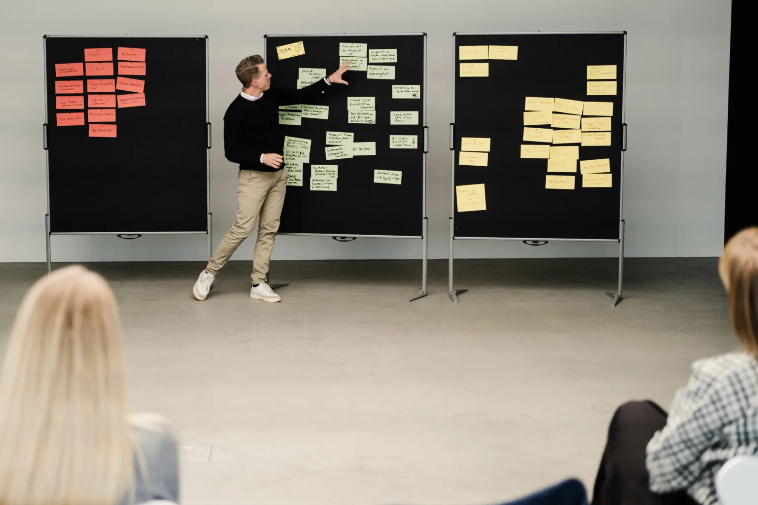 A speaker is presenting at the CRM roundtable in front of three pinboards covered with coloured sticky notes, while participants listen in the foreground.