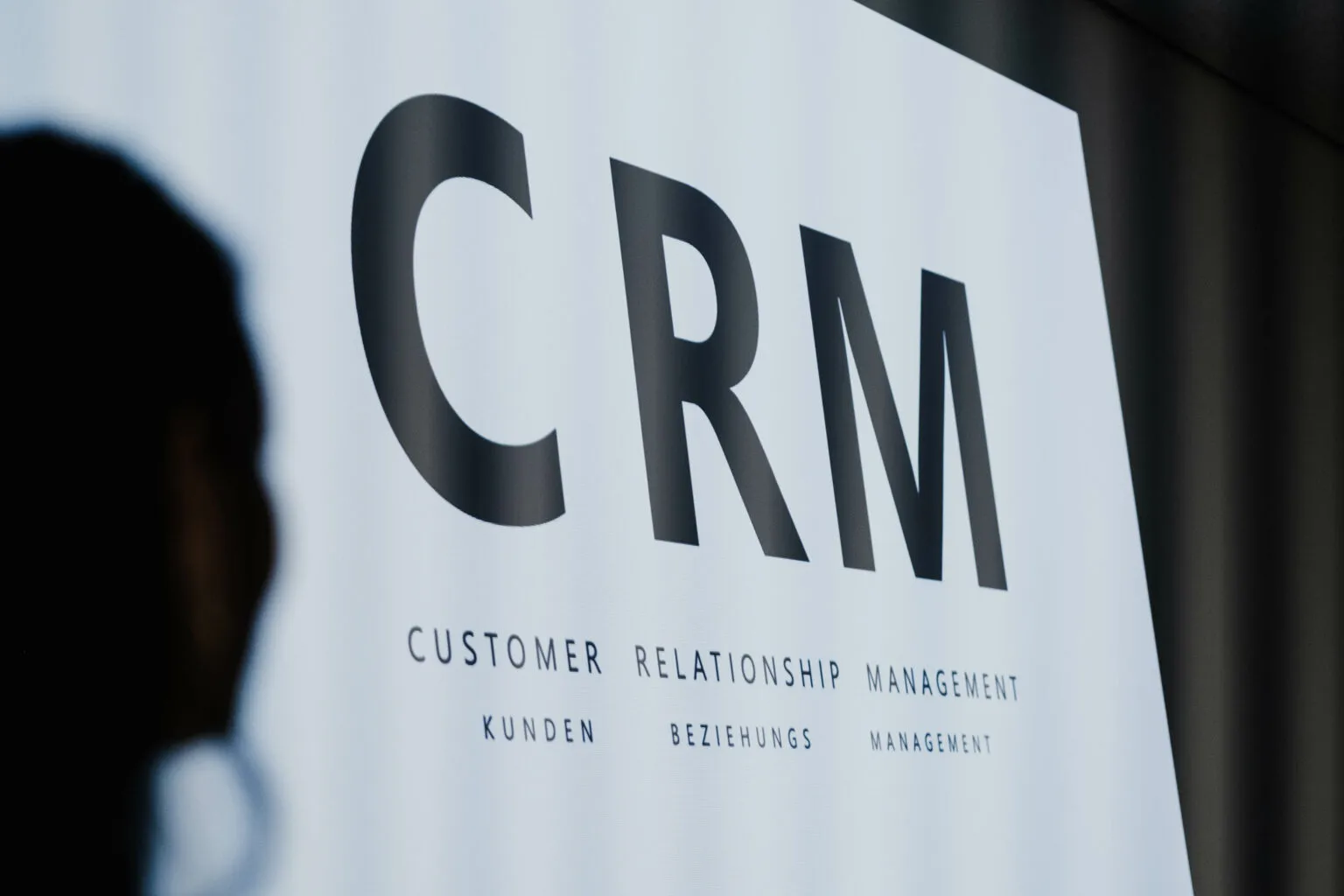 Large CRM presentation slide with the words “Customer Relationship Management” at the CRM roundtable, with a blurred person’s silhouette in the foreground.