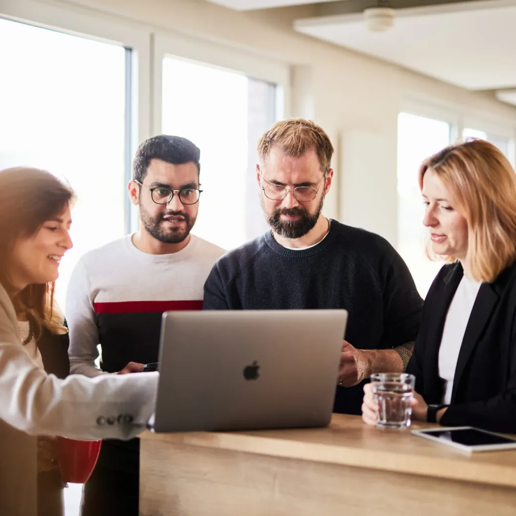 A group of colleagues looking at a laptop together and talking about a project.