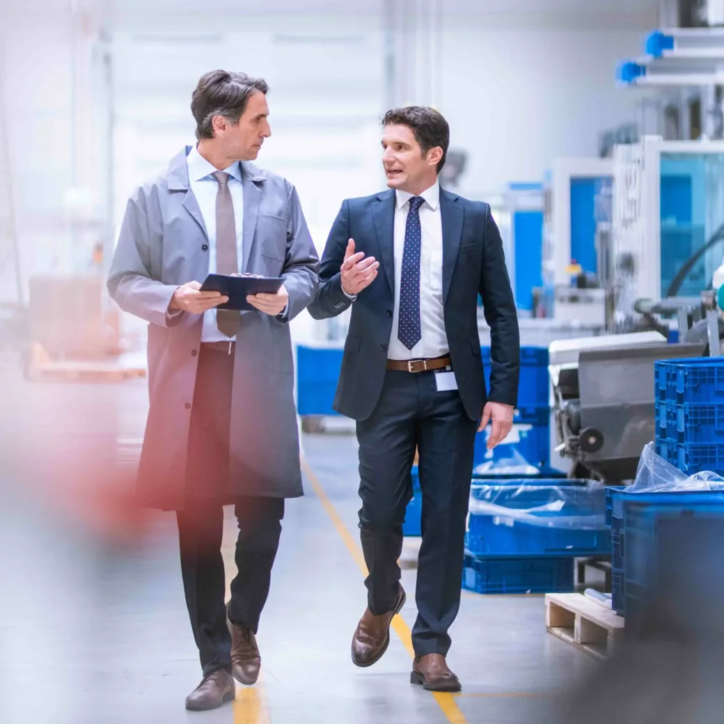 Zwei Männer laufen durch eine Produktionshalle und unterhalten sich