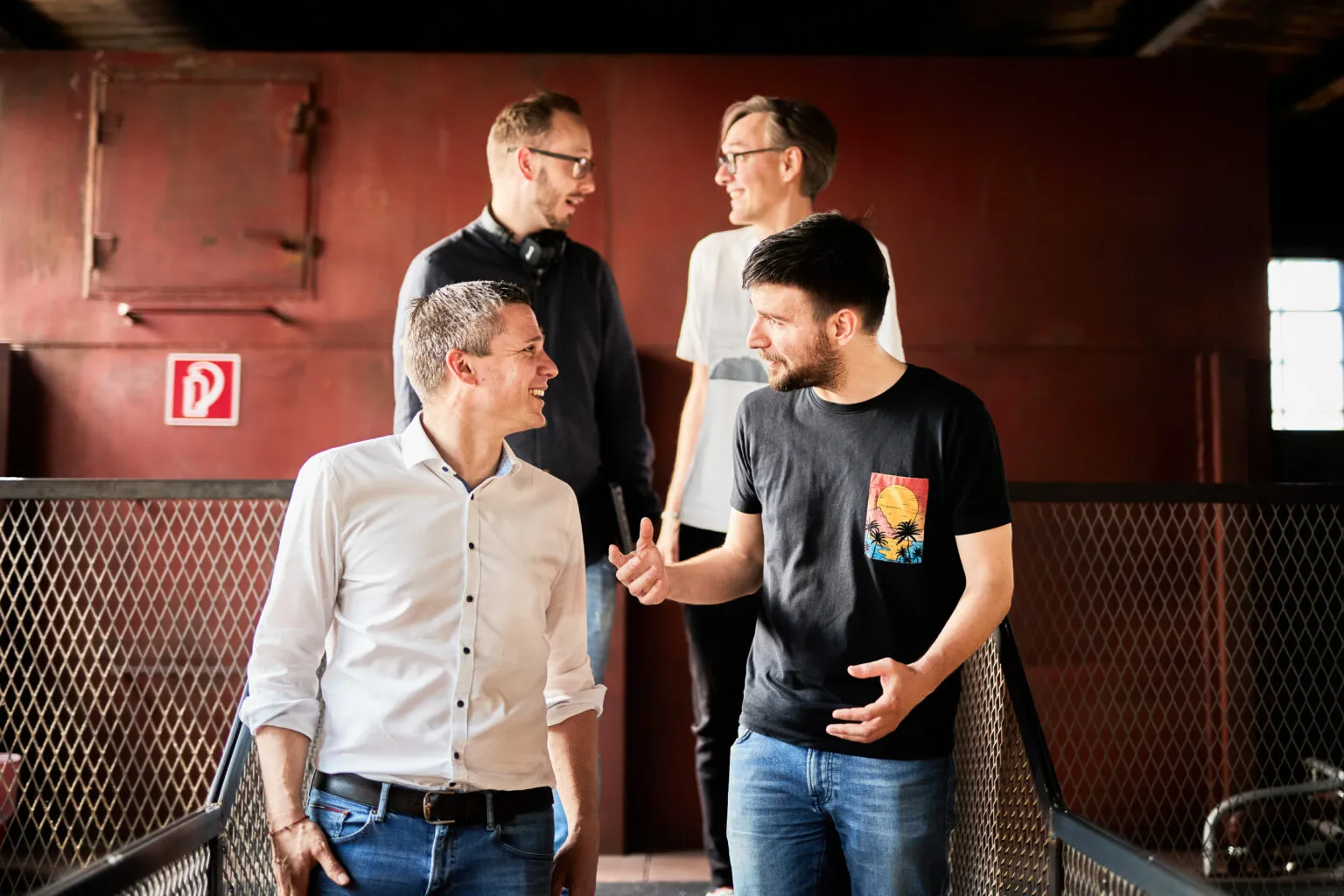 Foto von vier Kollegen, die sich unterhalten, während sie eine Eisentreppe runter gehen.