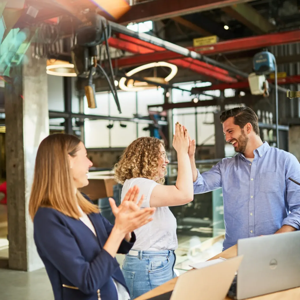 Foto von drei Kolleg*innen, die sich über ein abgeschlossenen Projekt freuen.