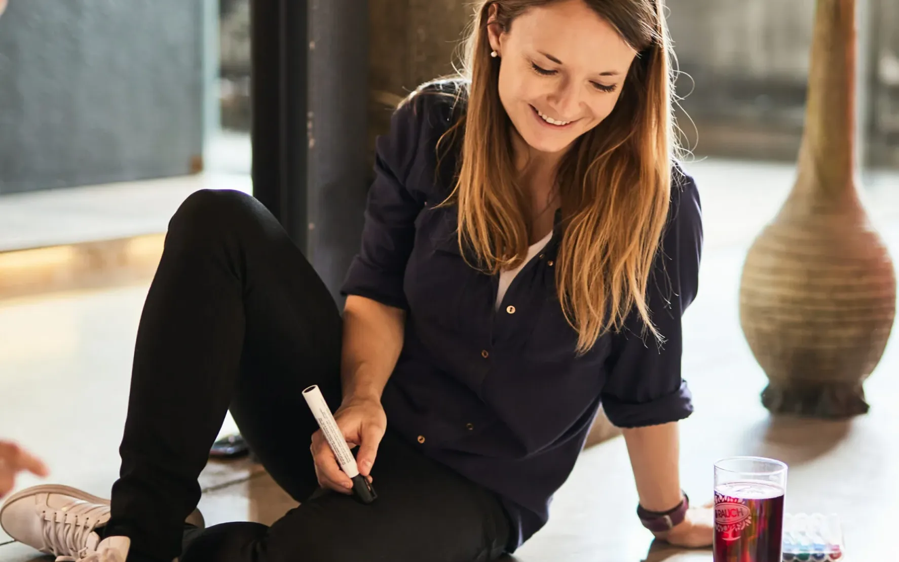 Foto von einer jungen Frau mit einem Stift in der Hand, die am Boden sitzt und an einem Plakat für ein Projekt arbeitet.