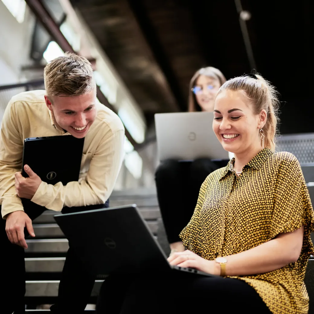 Photo of a young woman and a young man sitting on steps and working on a presentation on a laptop.