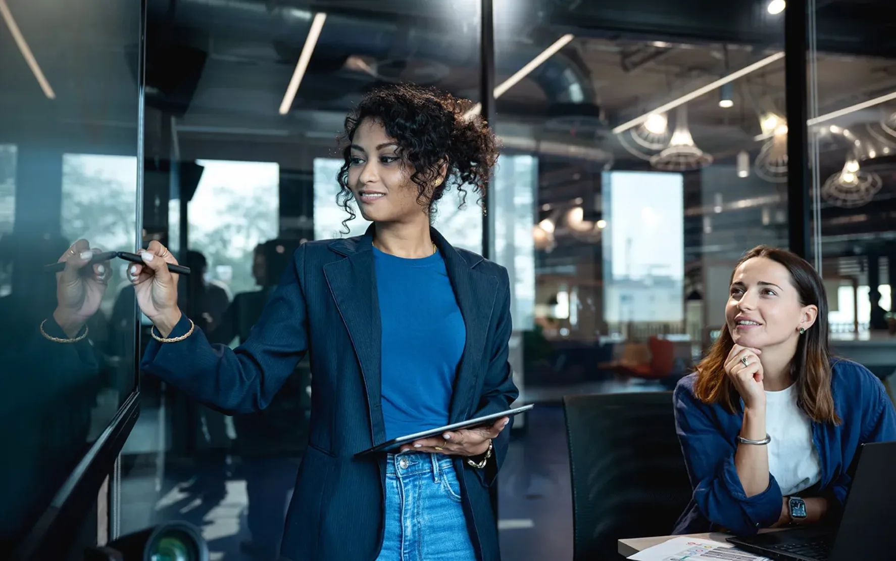 Frau mit dunklen Locken erklärt freundlich Inhalte auf einem Whiteboard im Büro