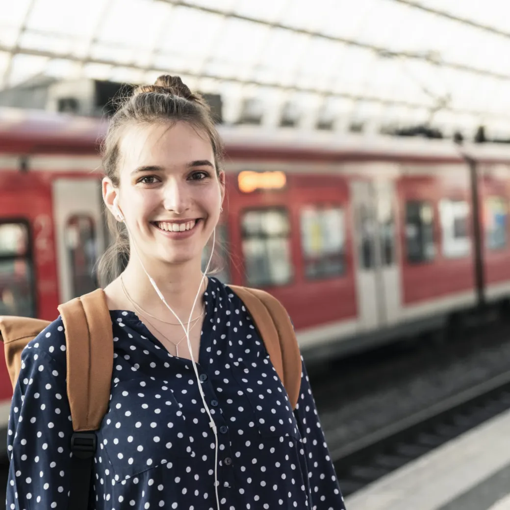 Porträt einer lächelnden jungen Frau am Bahnhof, Zug im Hintergrund