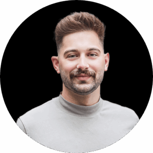 Ein Mann mit kurzen braunen Haaren, Schnurrbart und Bart, der einen hellgrauen Rollkragenpullover trägt, lächelt leicht vor einem schlichten schwarzen Hintergrund - aufgenommen während der valantischen dmexco-Veranstaltung.