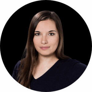 Eine Frau mit langen braunen Haaren und einem neutralen Gesichtsausdruck trägt ein dunkles Oberteil, das auf der dmexco2025 vor einem schlichten schwarzen Hintergrund abgebildet ist.