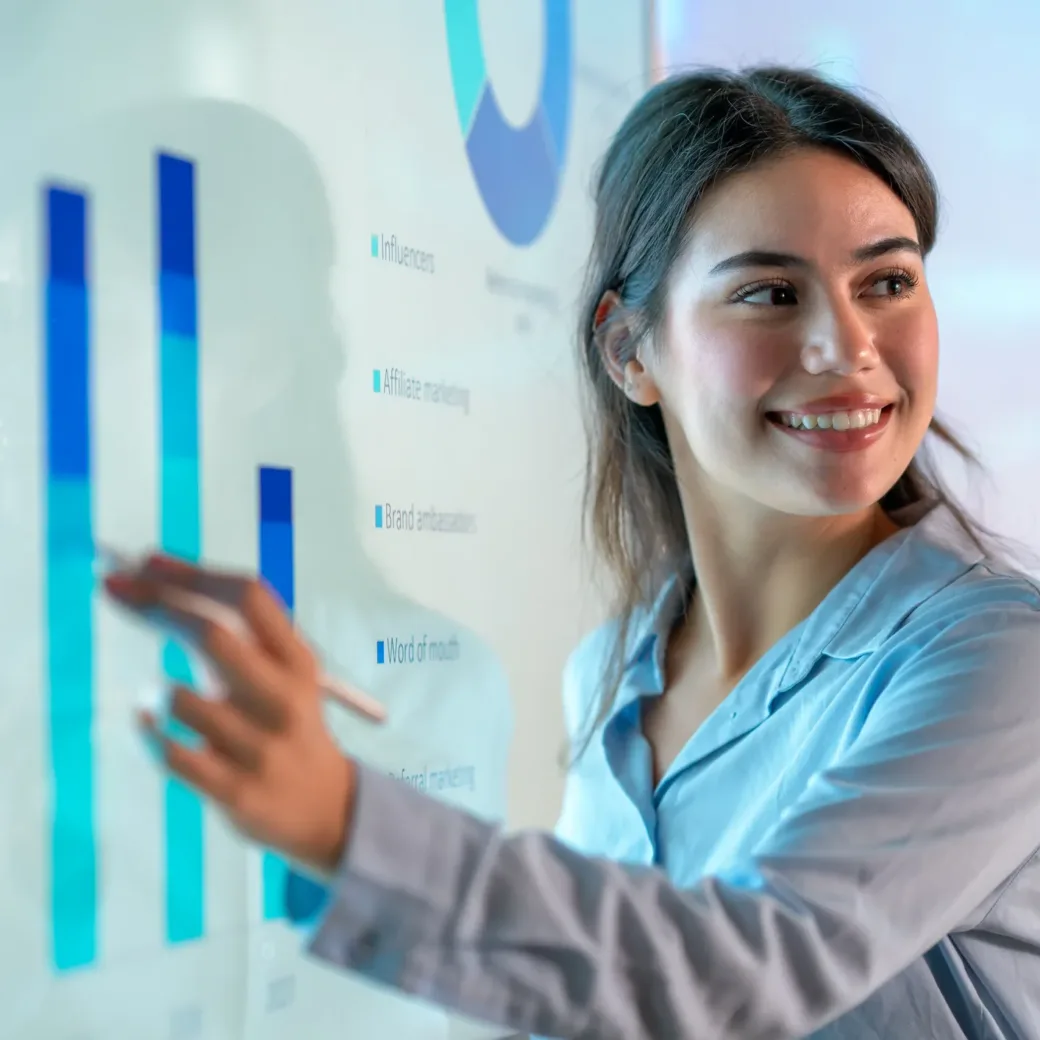 Eine Frau in einem blauen Hemd zeigt während einer Präsentation auf ein Balkendiagramm auf einem großen interaktiven Bildschirm und lächelt, während sie die Daten zur Digitalisierung in Versicherungen erläutert.