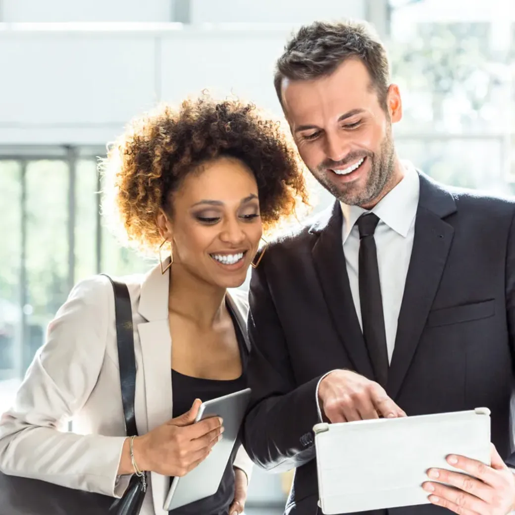 Cheerful businessman and businesswoman standing in an office hall and using a digital tablet totgether.
