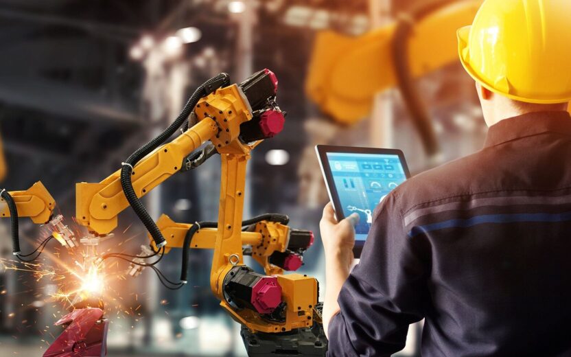 An employee in a manufacturing facility operates machines, robots, and equipment. The image symbolizes digital manufacturing and smart manufacturing.