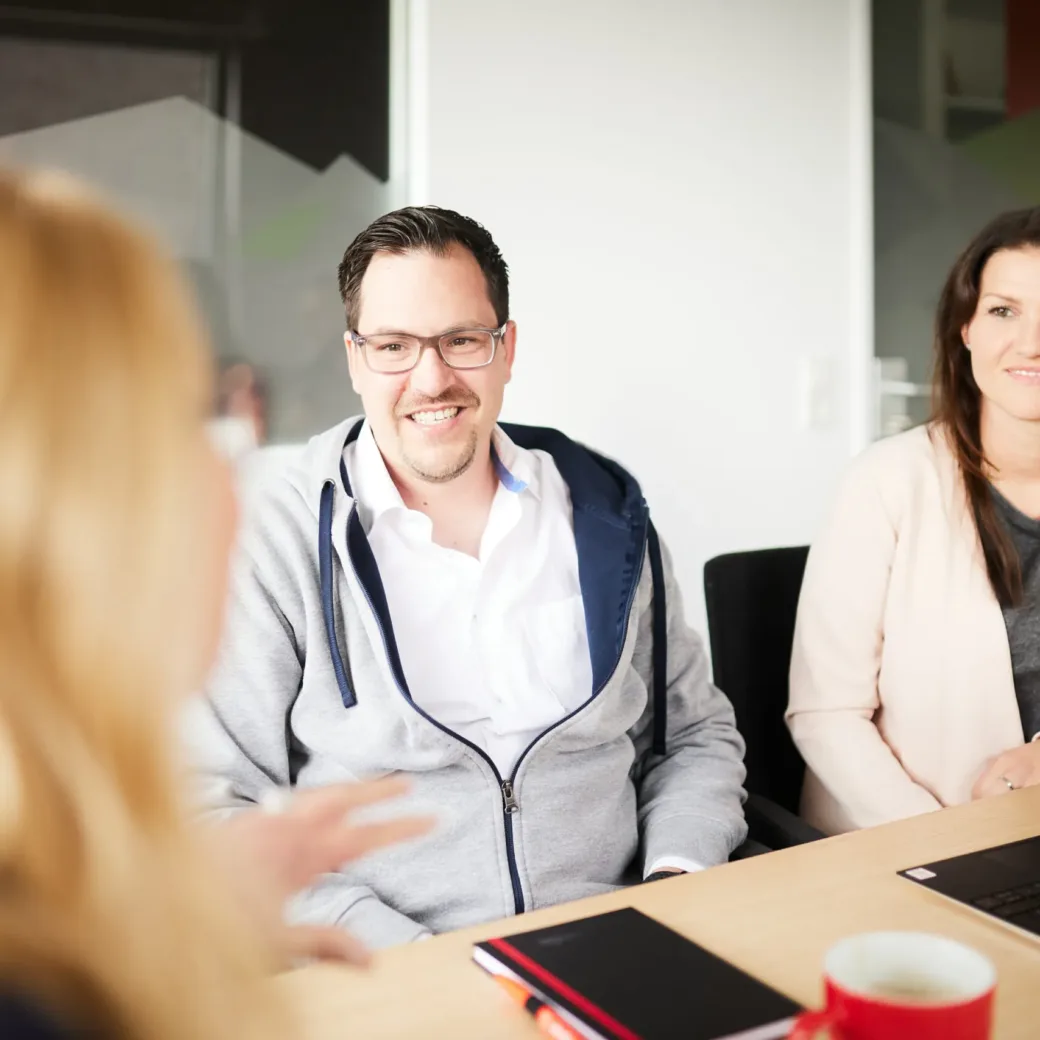 Photo of a man and a woman sitting at a conference table and being advised by a lady.