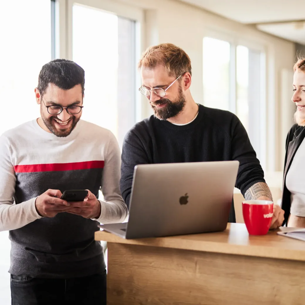 Vier Kollegen, die über ein Smartphone und einen Laptop ein Onlineshop-System testen.