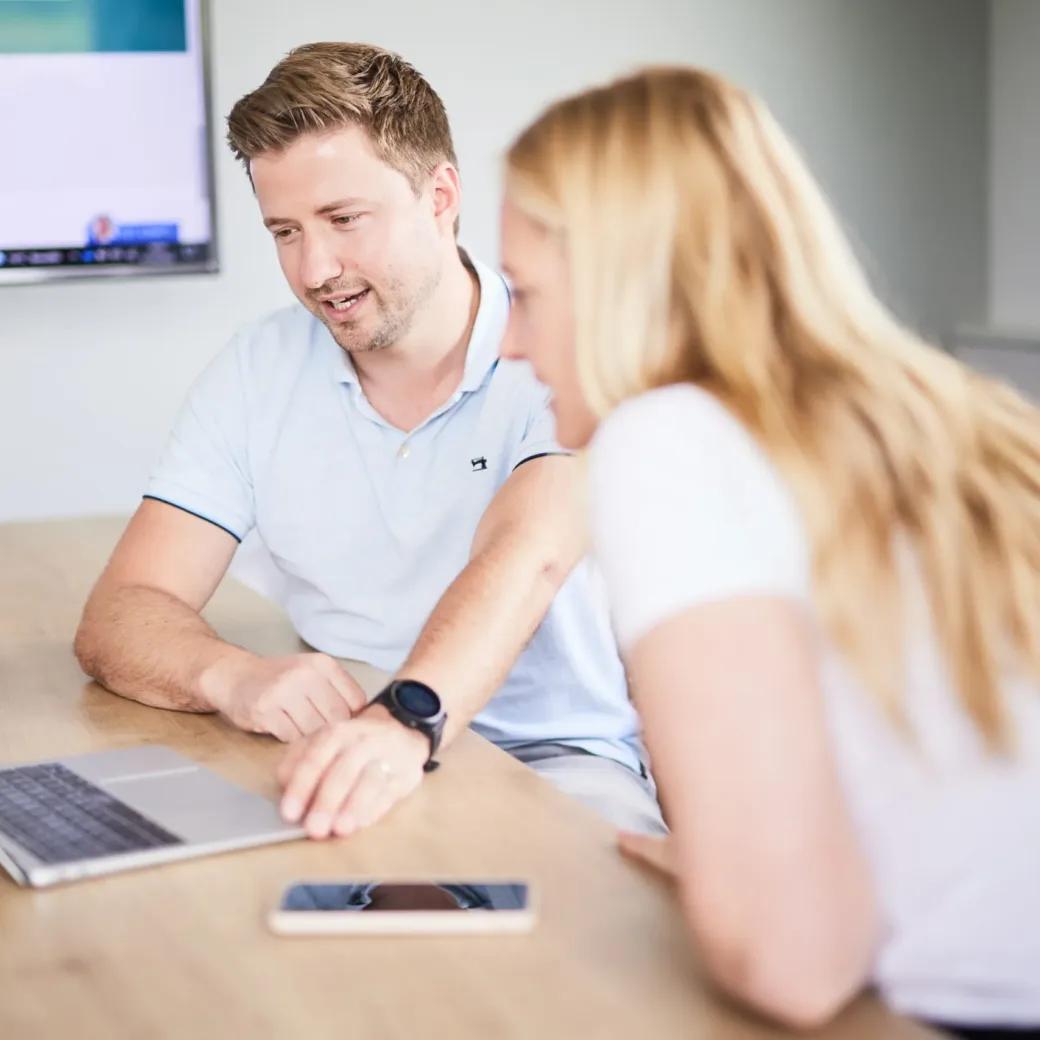 Bild von einem valantic CX-Mitarbeiter, der seiner Kollegin am Laptop aktuelle Daten einer Customer Journey erklärt.