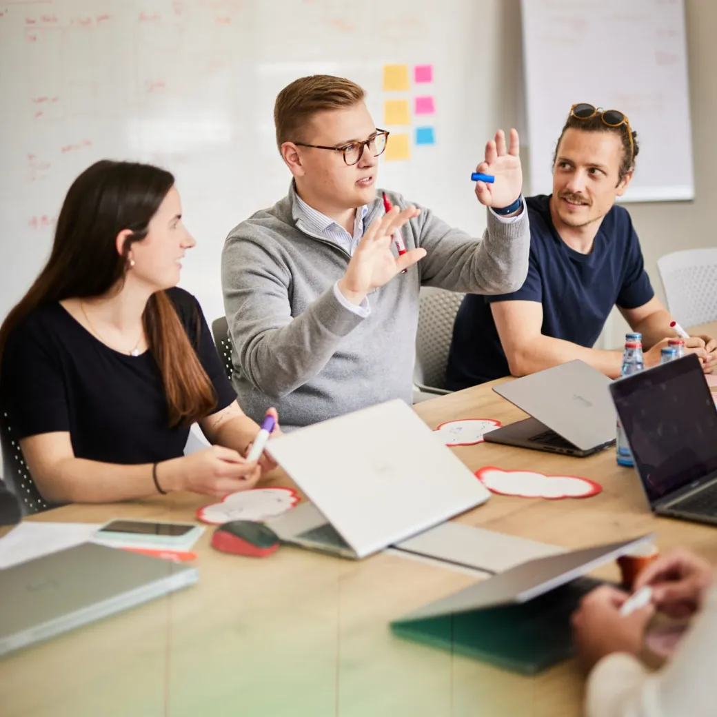 Foto von einem jungen Mann, der in einem Meeting etwas erklärt und dabei mit den Händen gestikuliert.