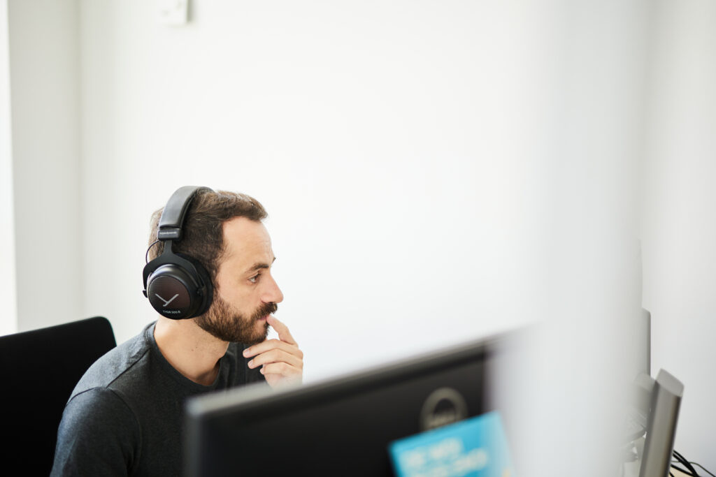 Bild von einem konzentrierten Mann am Büroarbeitsplatz, der Noice-Cancelling-Kopfhörer trägt.