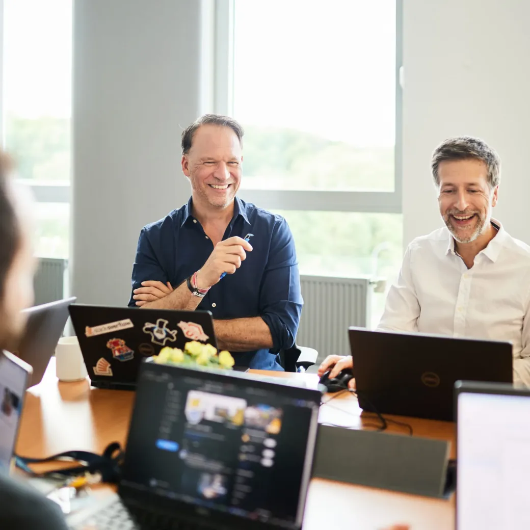 Foto von zwei Männern, die mit ihrem Laptop in einem Meeting sitzen.