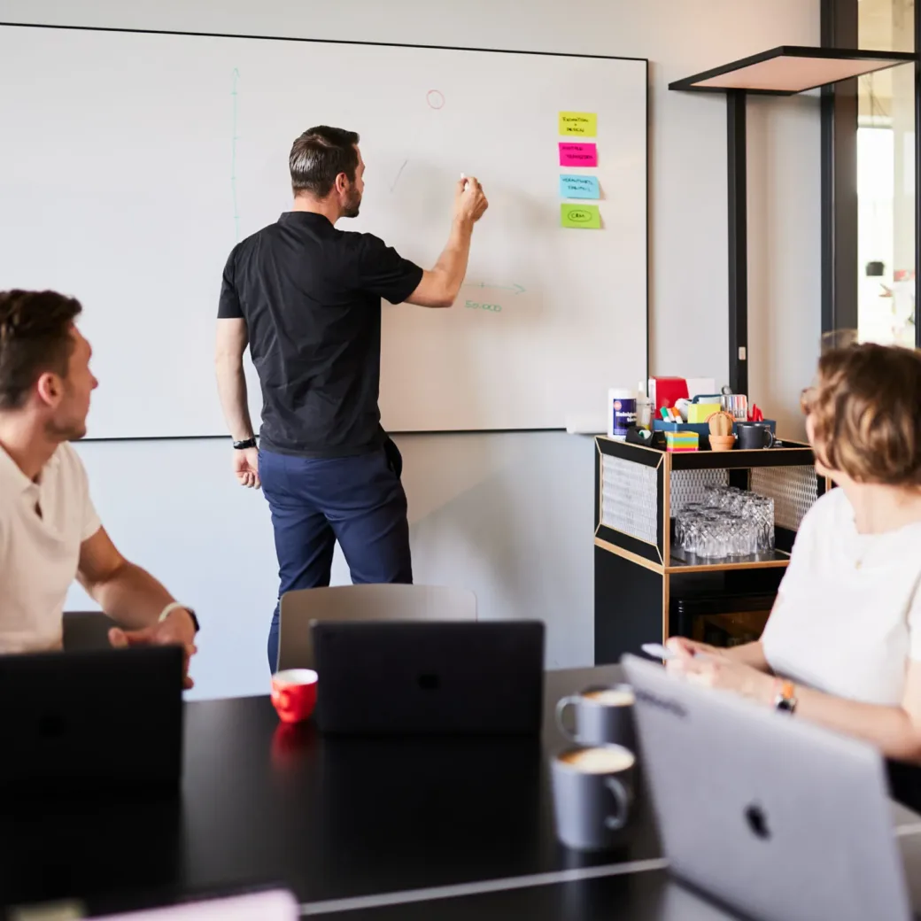 Photo of a man writing a formula on a whiteboard. He is facing away from the camera.