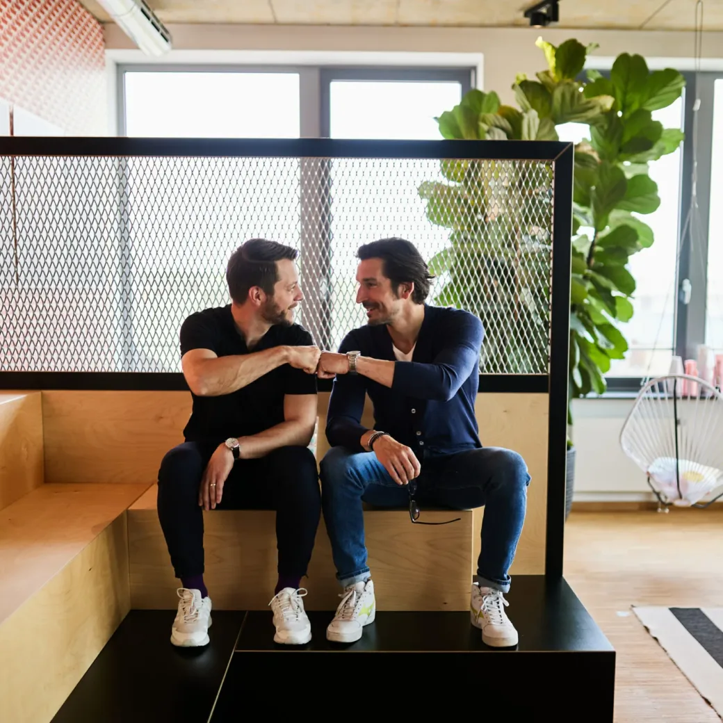 Two men sitting next to each other, fist-bumping.