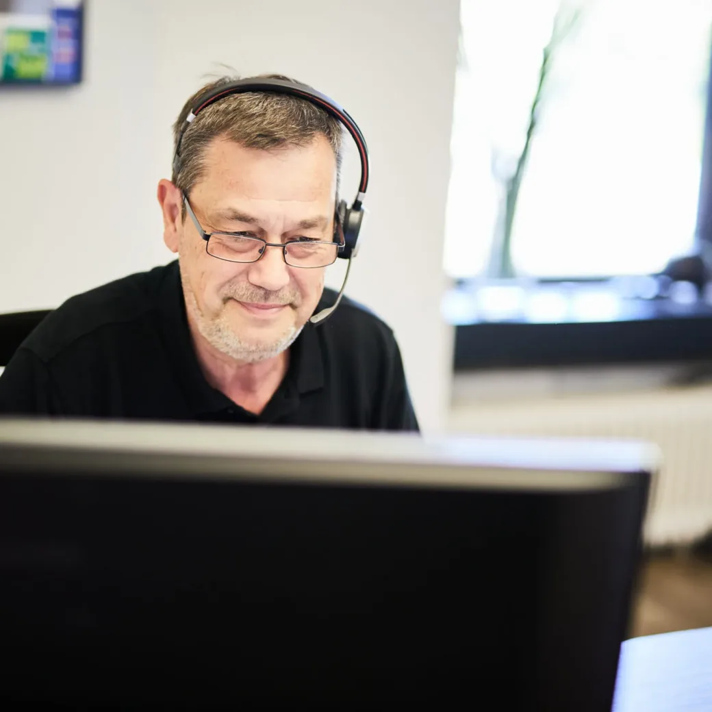 Photo of an older valantic CX employee wearing headphones and working intently at the computer.
