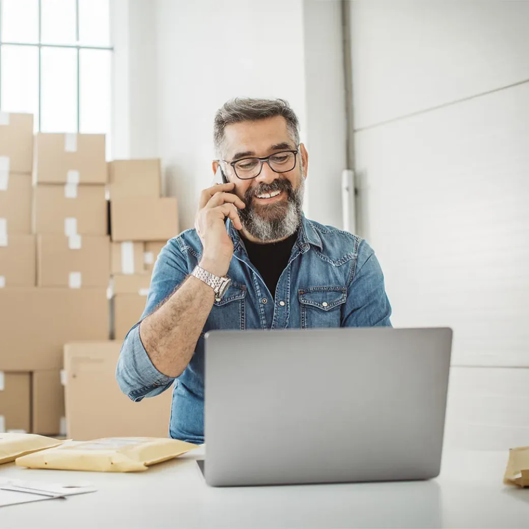 Bearded men working on packaging and online delivery in home office business. He talking on phone with customer