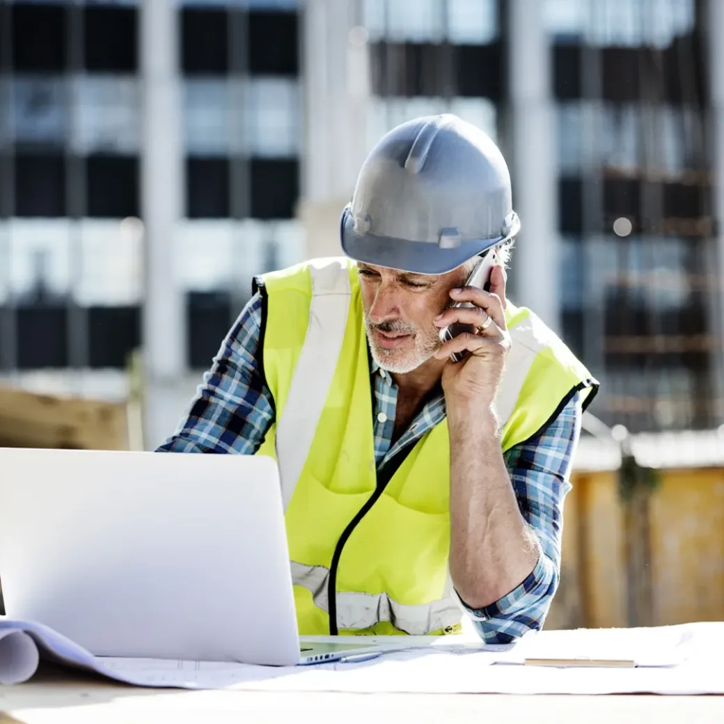 Homem arquiteto a usar um telemóvel e computador numa obra em construção