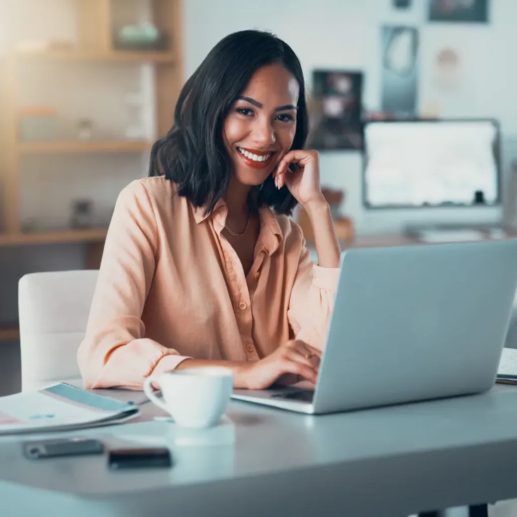 Portrait of a happy business woman working on her laptop at a desk in the office