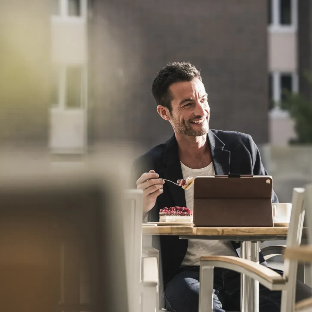 Ein Geschäftsmann der in einem Kaffee sitzt, Kuchen isst und Kaffee trinkt