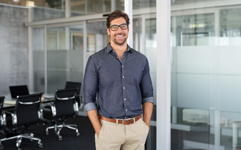 Portrait of young businessman wearing eyeglasses and standing outside conference room.