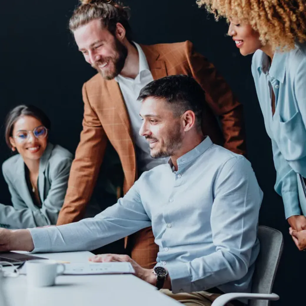 Team of four colleagues using a laptop computer together at office desk and talking about SAP S/4HANA.