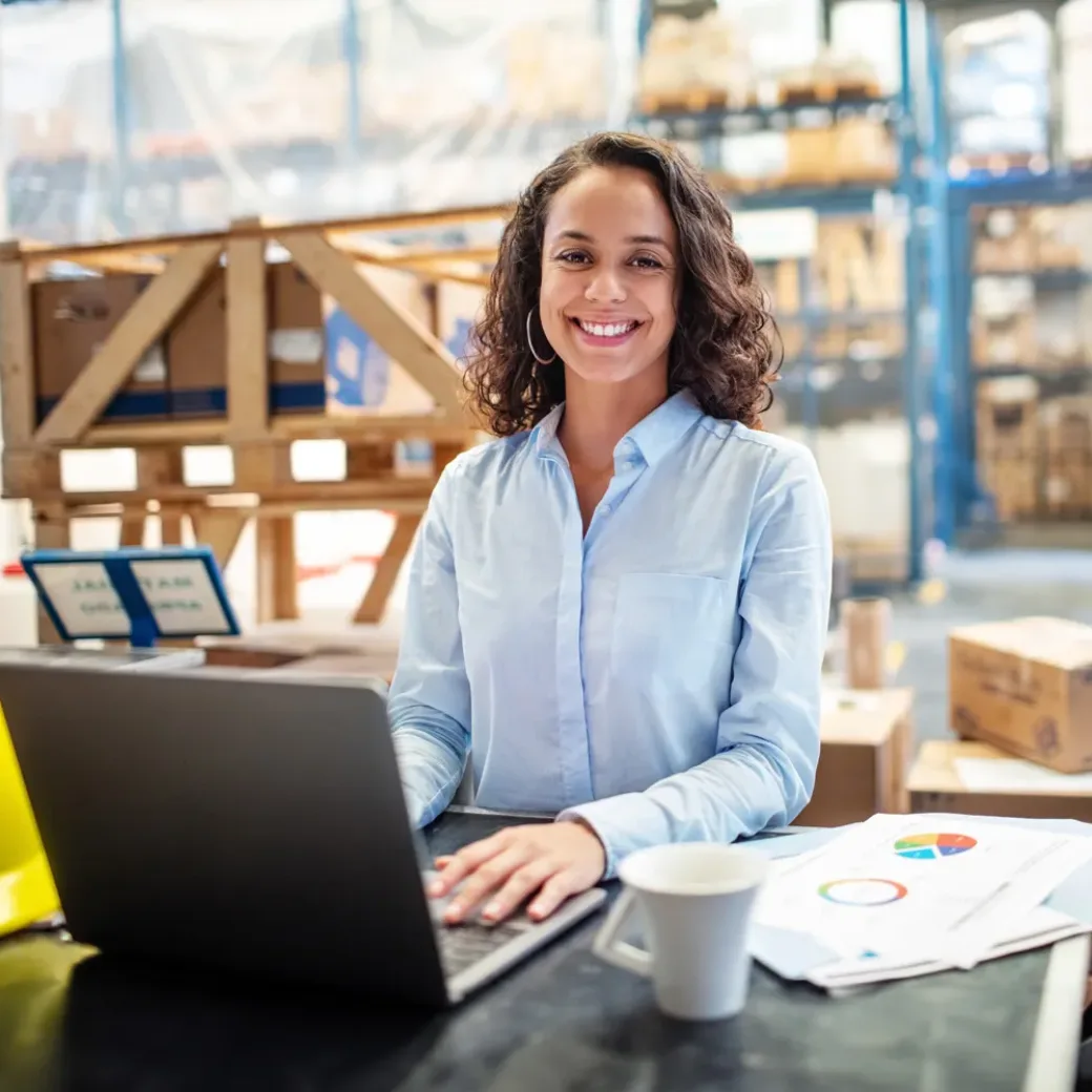 Smiling business woman working on laptop at a warehouse. Businesswoman with a laptop working at a distribution warehouse.