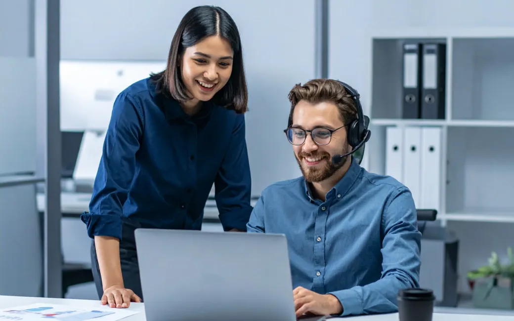 coding specialist working in an office on his laptop. with a headset on smiling.