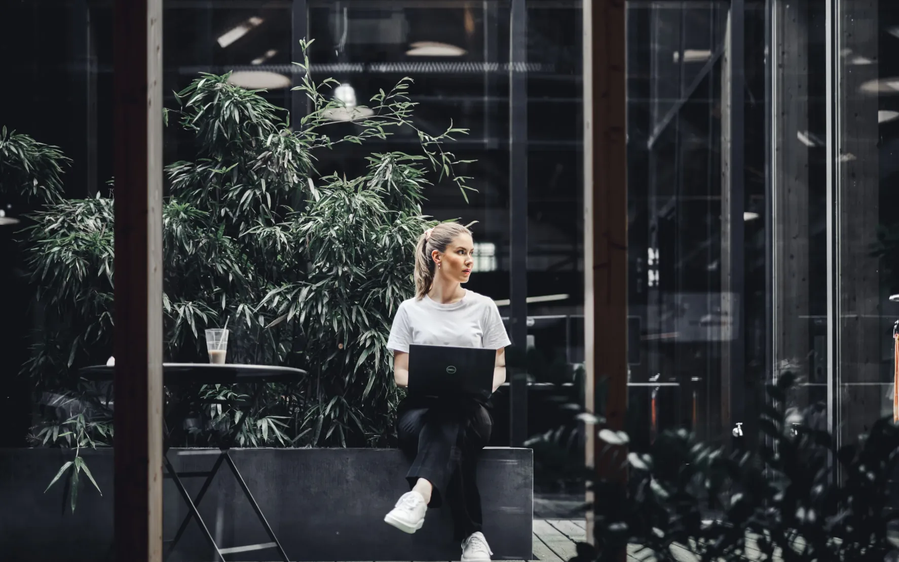 Junge valantic Austria Mitarbeiterin, die mit ihrem Laptop in einem kleinen Wintergarten sitzt und an einem Projekt arbeitet.