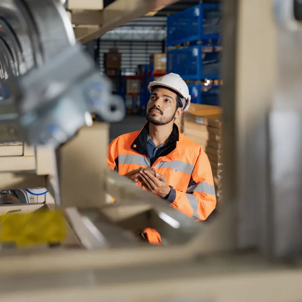 Jovem engenheiro industrial com um capacete branco a verificar a soldadura na linha de produção da fábrica.