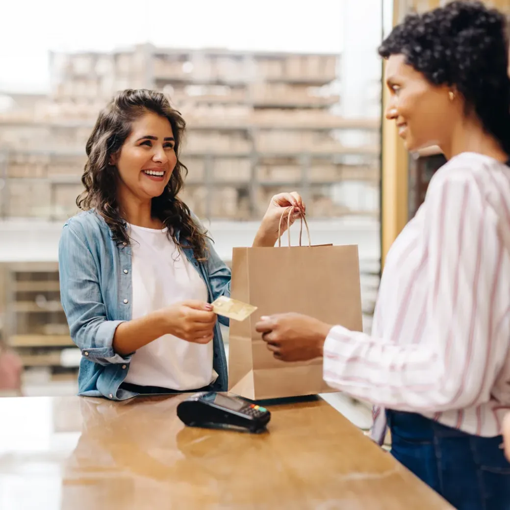 Mulher jovem e alegre a sorrir enquanto faz compras numa pequena empresa local detida por mulheres.