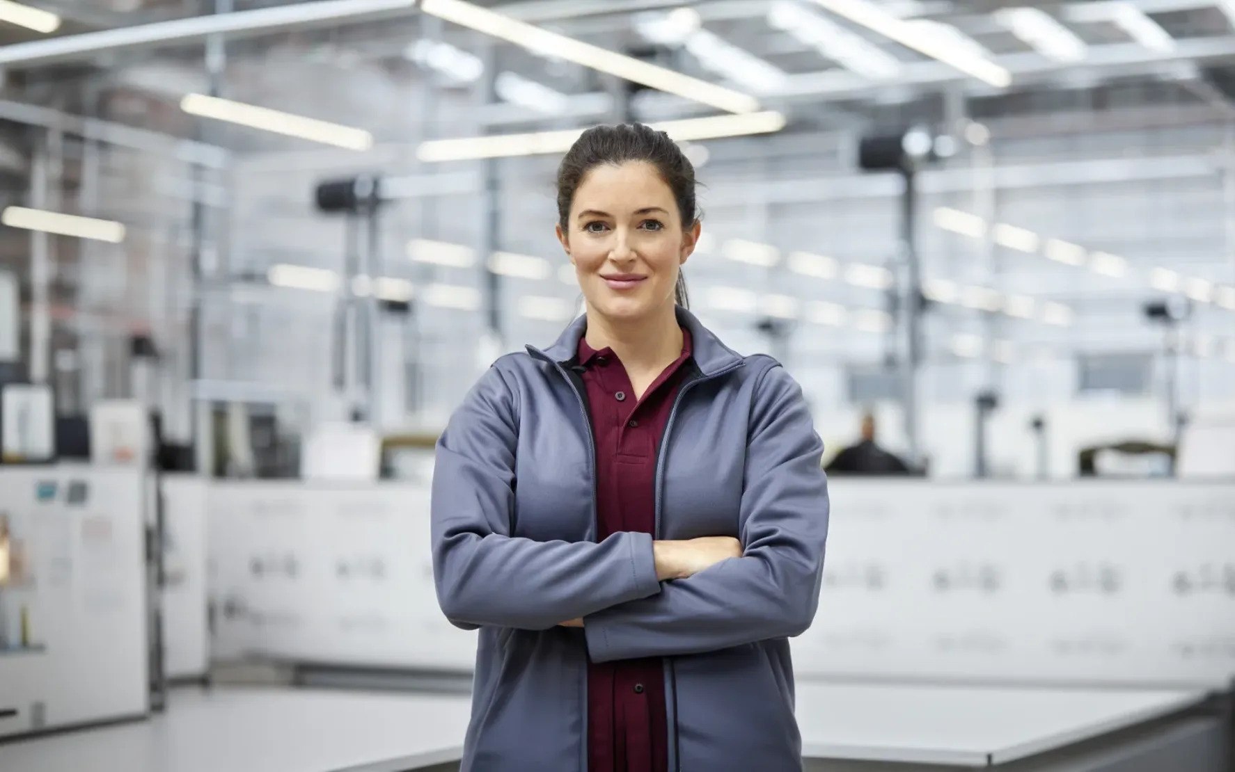 Portrait of female engineer with arms crossed in automobile industry. Confident technologist is standing in showroom. She is in jacket at factory.