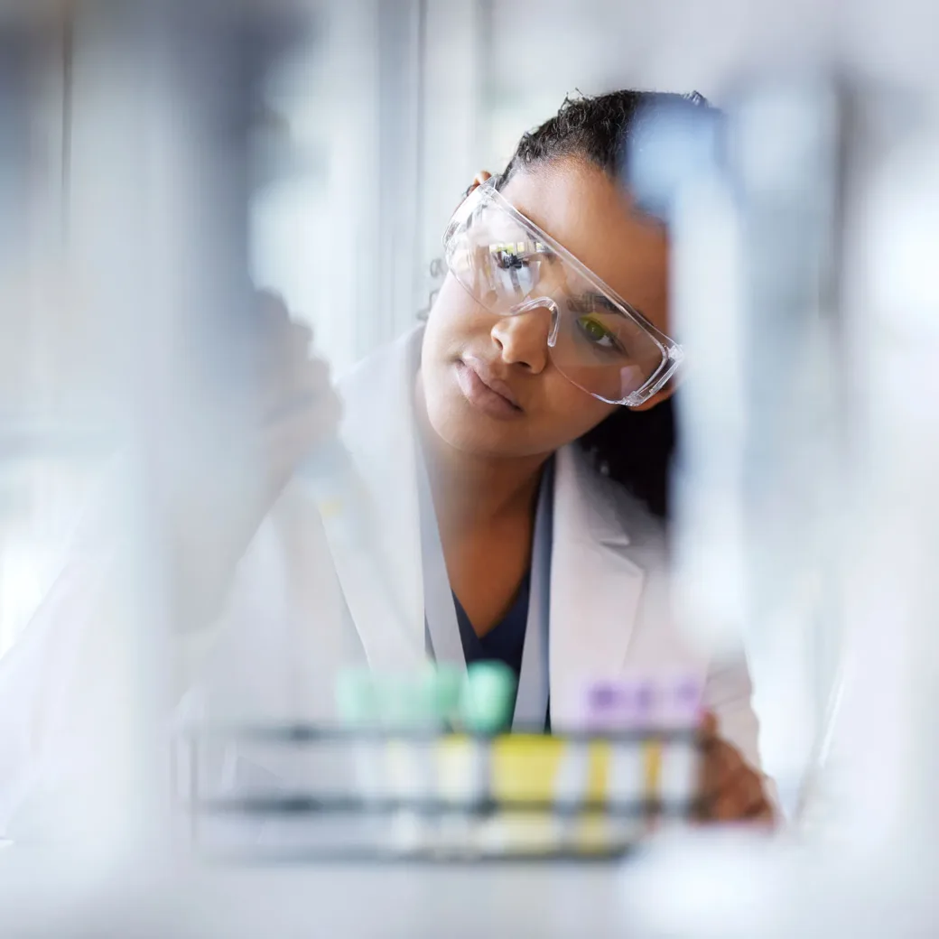 Ein Wissenschaftler, der eine Schutzbrille und einen Laborkittel trägt, arbeitet mit Reagenzgläsern in einer Laborumgebung.