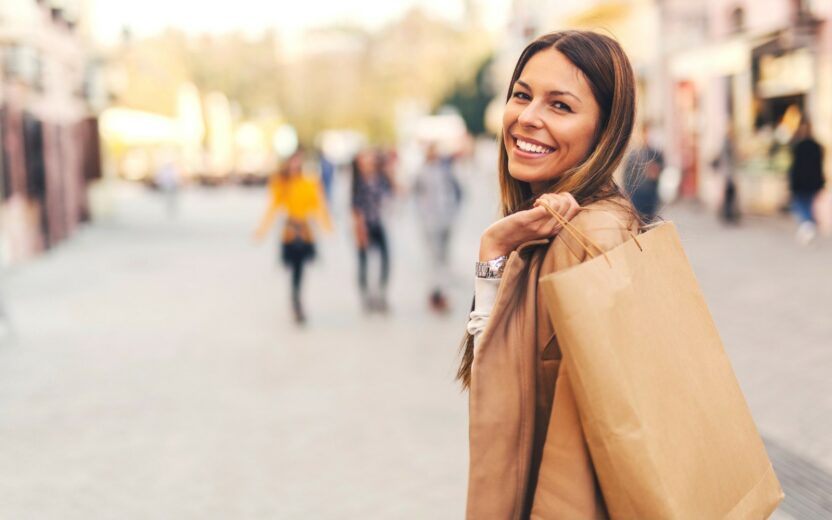 Bild von einer lächelnden Frau mit Shoppingtüte in einer Fußgängerzone