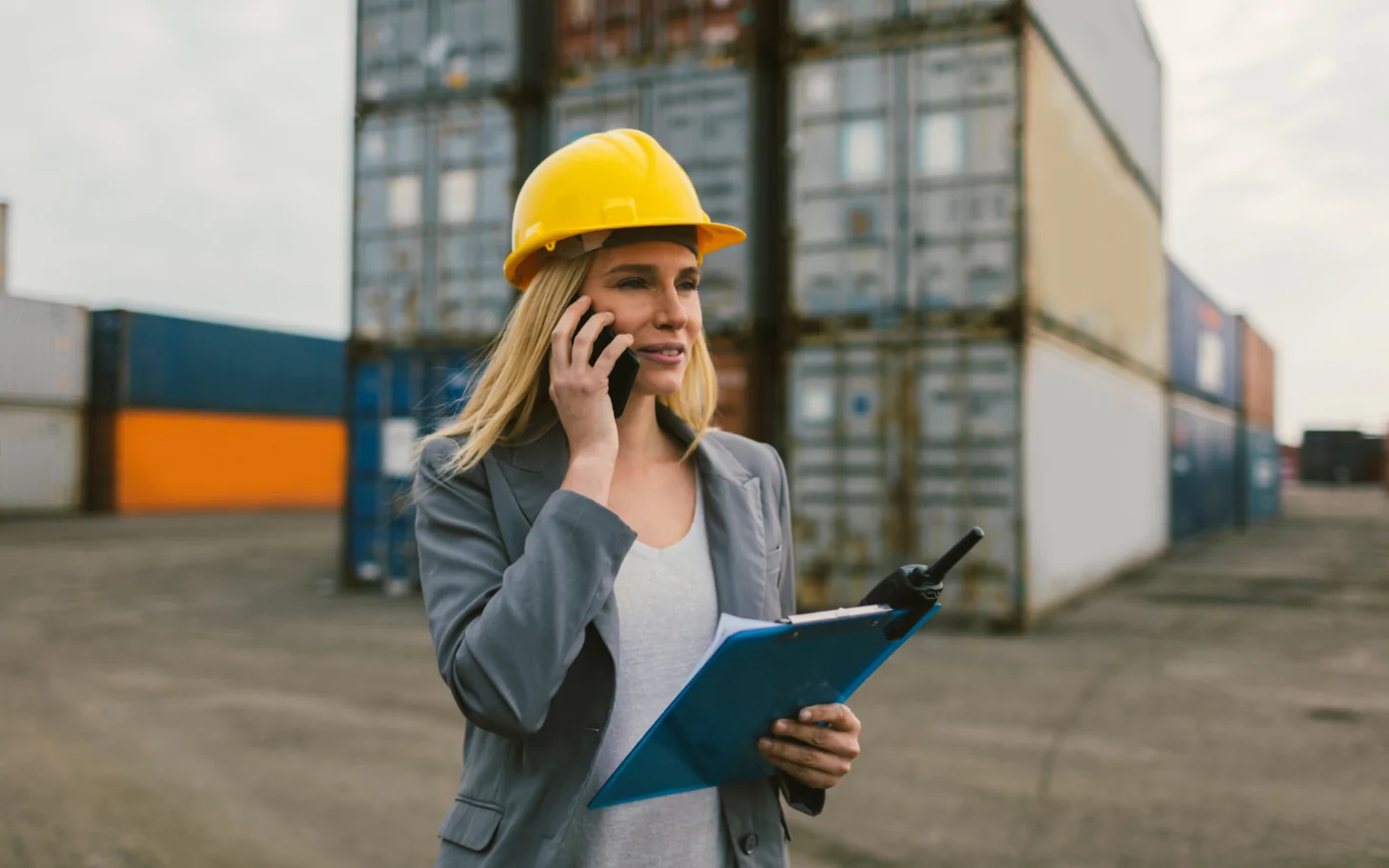 Frau mit Bauhelm am Telefon in einem Industriehafen