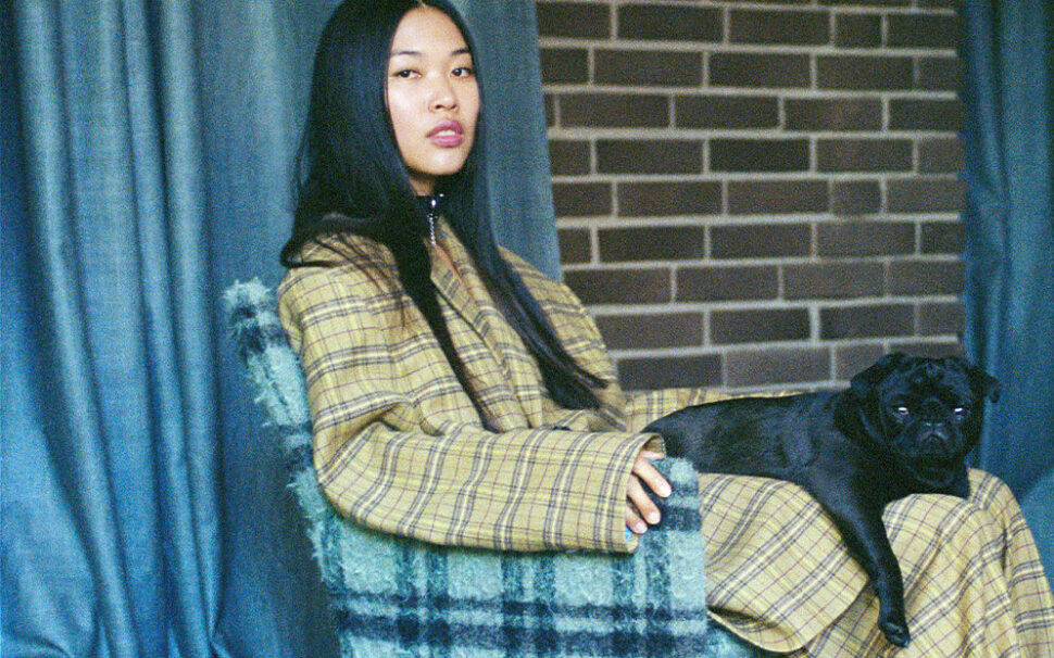 Bild von einer jungen Frau in Designerklamotten, die einen schwarzen Mops auf ihrem Schoß hat.