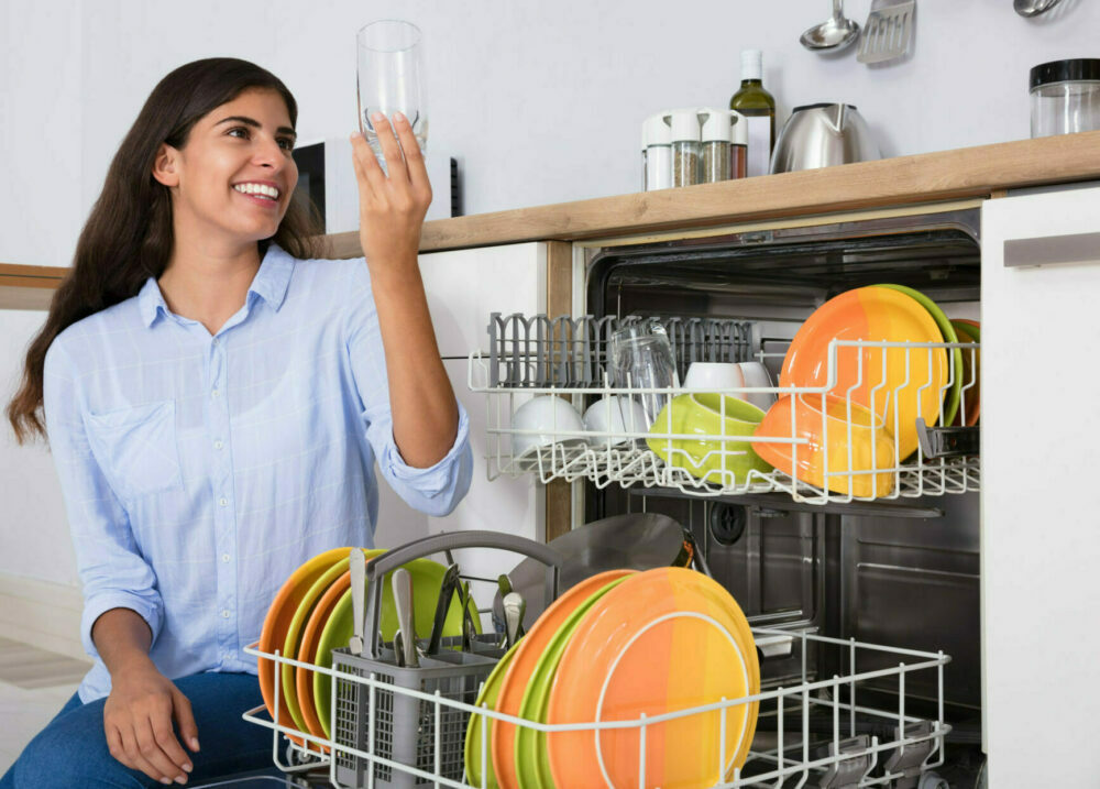 Woman looking at washed glass in front of dishwasher and smiling