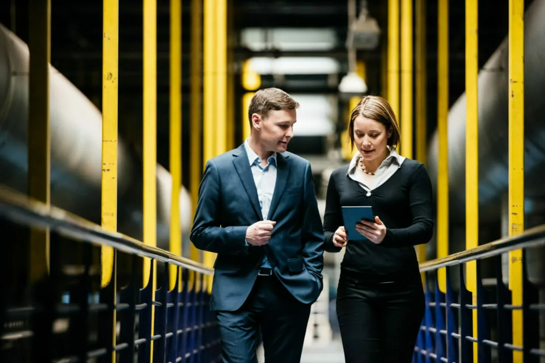Two business people walk through production hall looking at a tablet