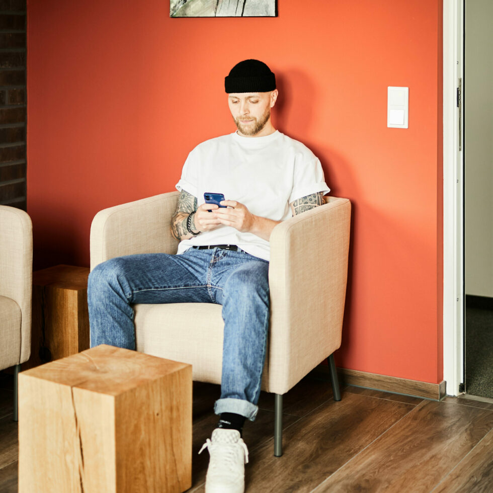 Foto von einem valantic CX-Mitarbeiter, der lässig in einem bequemen Stuhl sitzt und auf seinem Smartphone schaut.