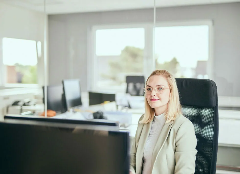 Foto von einer jungen Frau mit Brille, die an ihrem Büro-Arbeitsplatz sitzt.